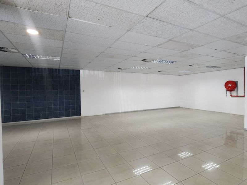 An open-plan retail space featuring ceramic tiled flooring, a suspended ceiling with recessed lighting, and a wall-mounted fire hose reel.
