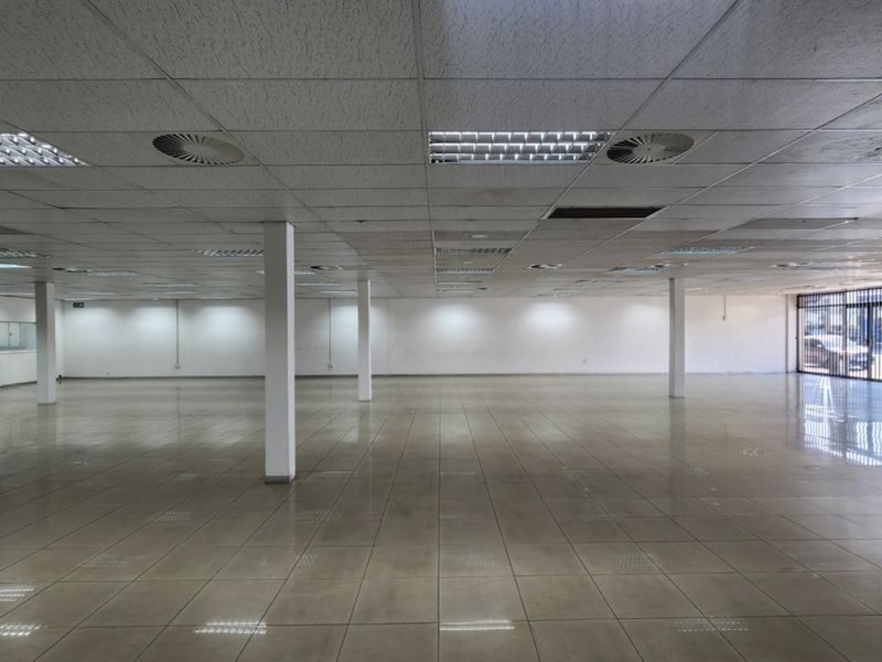 A spacious, open-plan retail unit featuring ceramic floor tiles, a suspended ceiling with recessed lighting, and structural support columns.