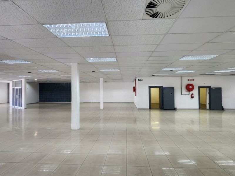 A spacious, open-plan retail area featuring tiled flooring, a suspended ceiling with recessed lighting, and multiple secure access points.
