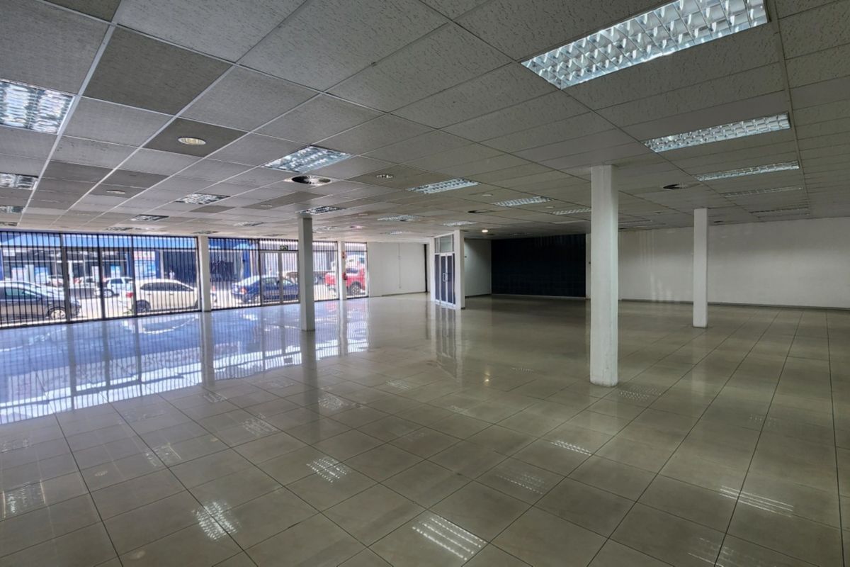 Spacious open-plan retail area featuring tiled flooring, suspended ceilings with recessed lighting, and large street-facing security gates.