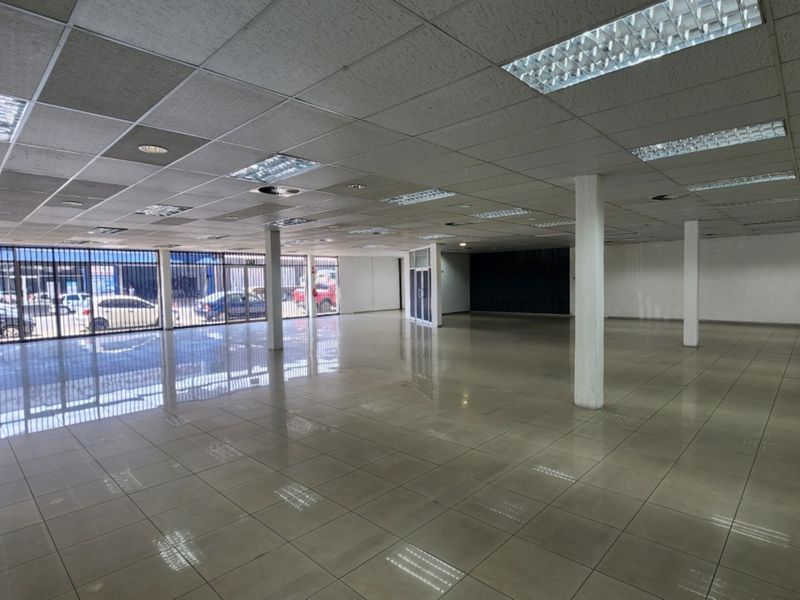 Spacious open-plan retail area featuring tiled flooring, suspended ceilings with recessed lighting, and large street-facing security gates.