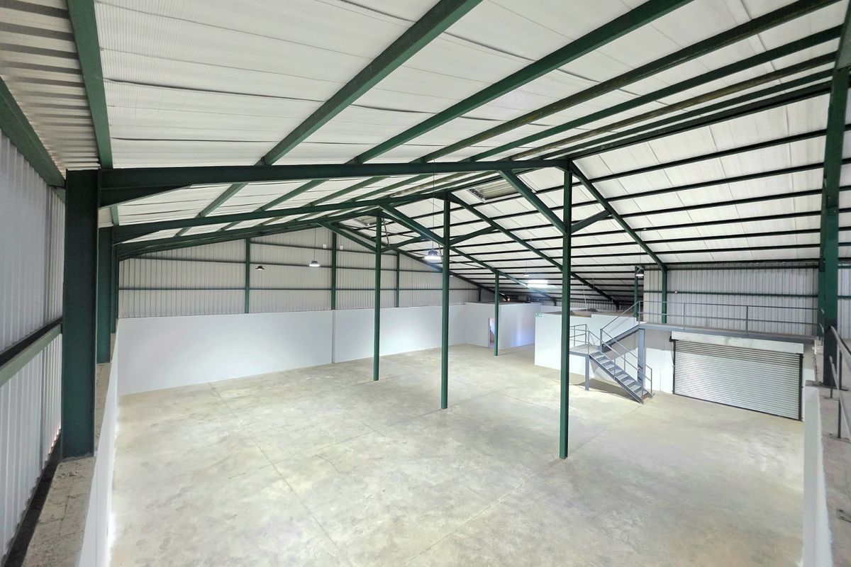 Spacious industrial warehouse unit featuring a high-clearance steel portal frame, concrete flooring, mezzanine level with staircase, and a large roller shutter door.