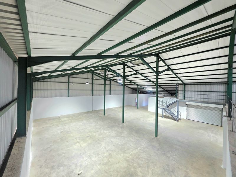 Spacious industrial warehouse unit featuring a high-clearance steel portal frame, concrete flooring, mezzanine level with staircase, and a large roller shutter door.