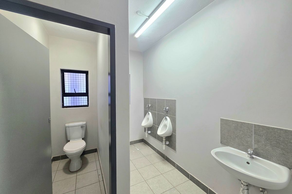 Clean industrial-style communal bathroom featuring wall-mounted urinals, a basin, and a separate toilet cubicle with tiled flooring and functional lighting.