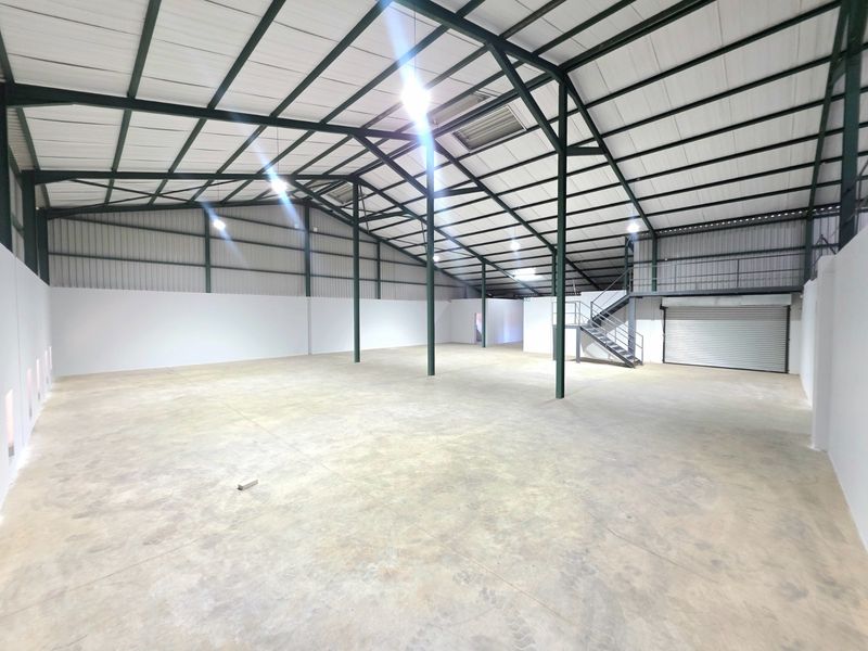Spacious industrial warehouse unit featuring high ceilings with exposed steel trusses, concrete flooring, a roller shutter door, and a mezzanine level.