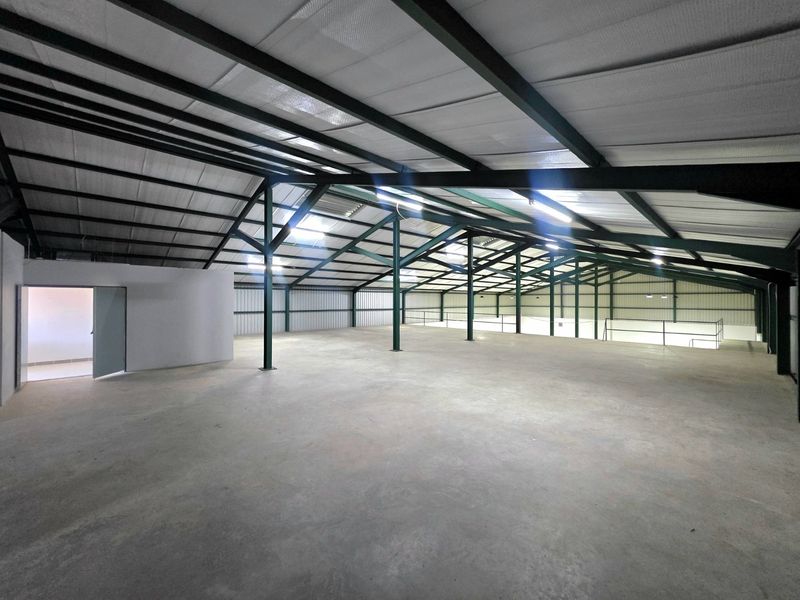 Spacious industrial warehouse interior featuring high ceilings with exposed steel trusses, concrete flooring, and metal wall cladding, suitable for storage or manufacturing.
