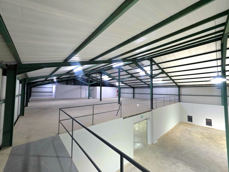 Spacious industrial warehouse interior featuring a mezzanine level, exposed steel roof trusses, and durable concrete flooring, suitable for storage or manufacturing operations.