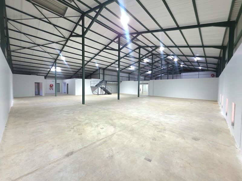 Spacious industrial warehouse unit featuring high ceilings, exposed steel portal frame, concrete flooring, and a mezzanine access staircase.