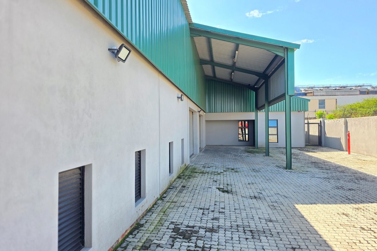 Rear exterior view of an industrial property featuring a covered loading area, paved driveway, and secure metal-clad facade with external lighting.