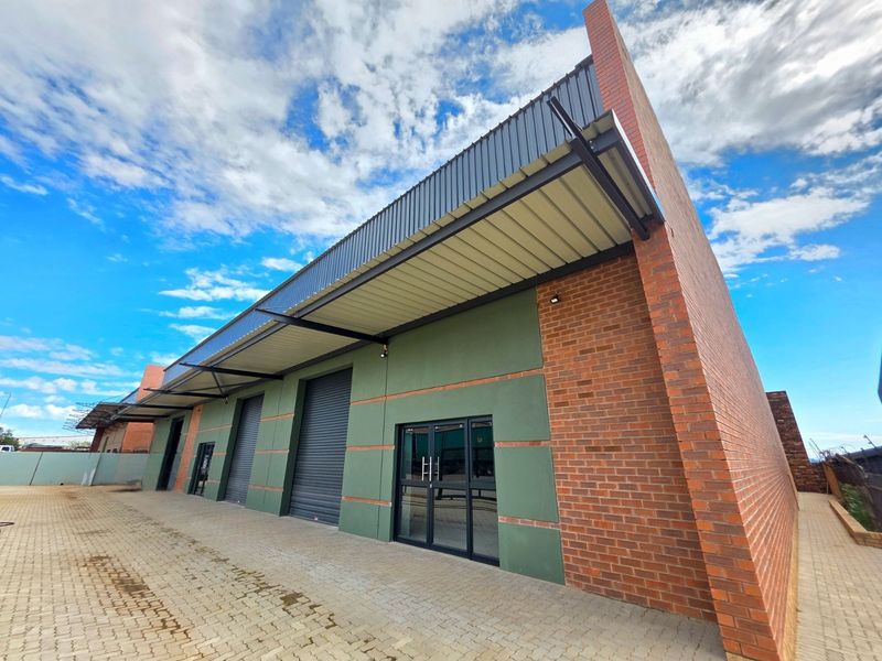 Modern industrial unit featuring a brick facade, roller shutter doors, and a metal roof canopy with a paved exterior approach.