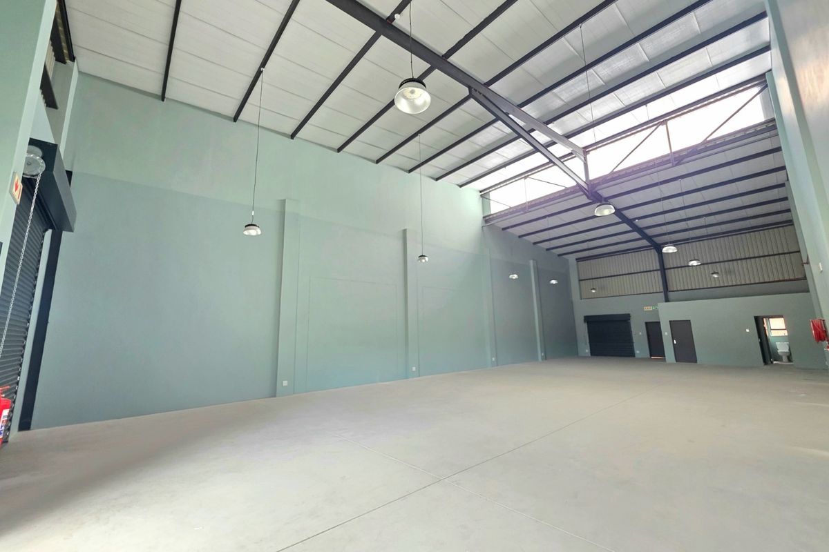 Spacious industrial warehouse unit featuring high ceilings with exposed steel trusses, polished concrete flooring, roller shutter access, and ample natural light via skylights.