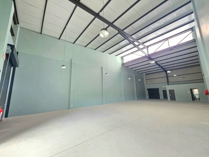 Spacious industrial warehouse unit featuring high ceilings with exposed steel trusses, polished concrete flooring, roller shutter access, and ample natural light via skylights.