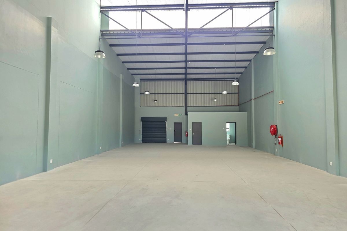 Spacious industrial warehouse unit featuring high ceilings with exposed steel trusses, concrete flooring, roller shutter access, and integrated fire safety equipment.