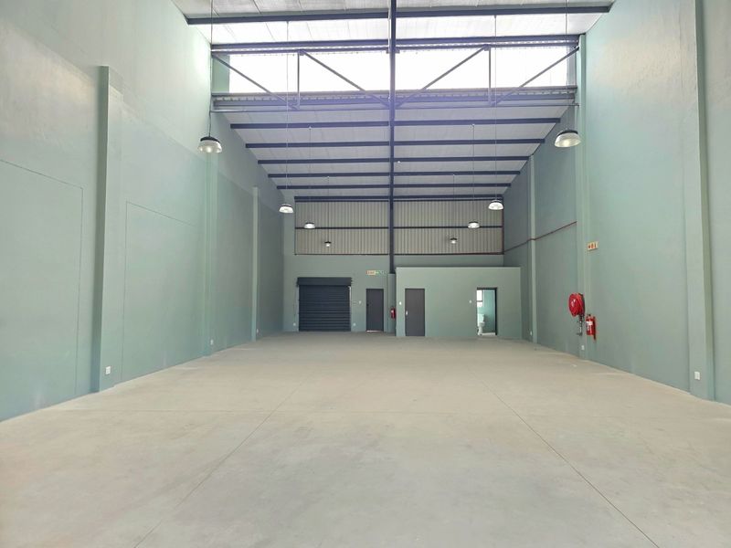 Spacious industrial warehouse unit featuring high ceilings with exposed steel trusses, concrete flooring, roller shutter access, and integrated fire safety equipment.