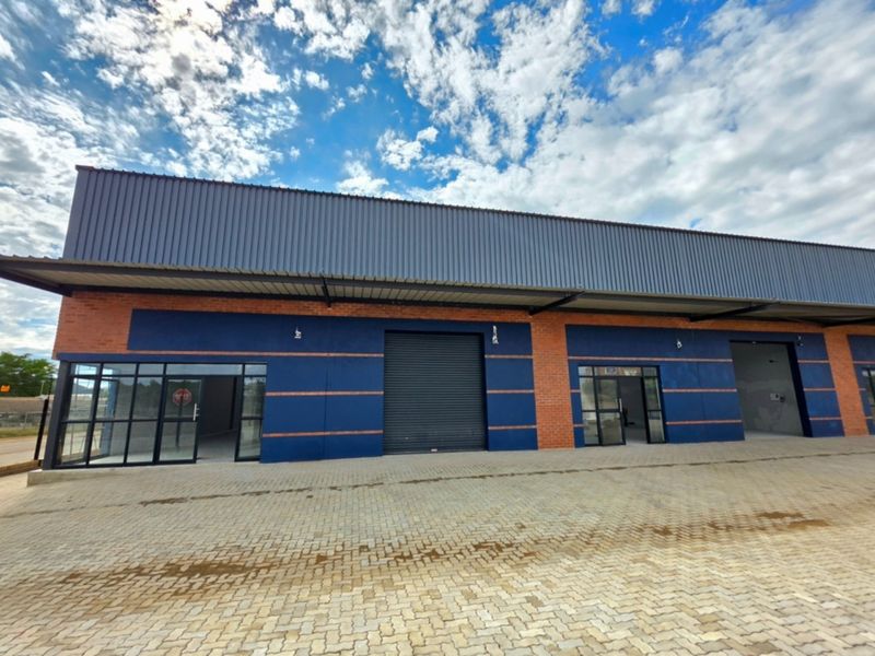 Modern industrial unit featuring a brick and metal facade, roller shutter door, and glass storefront entrance with paved exterior access.