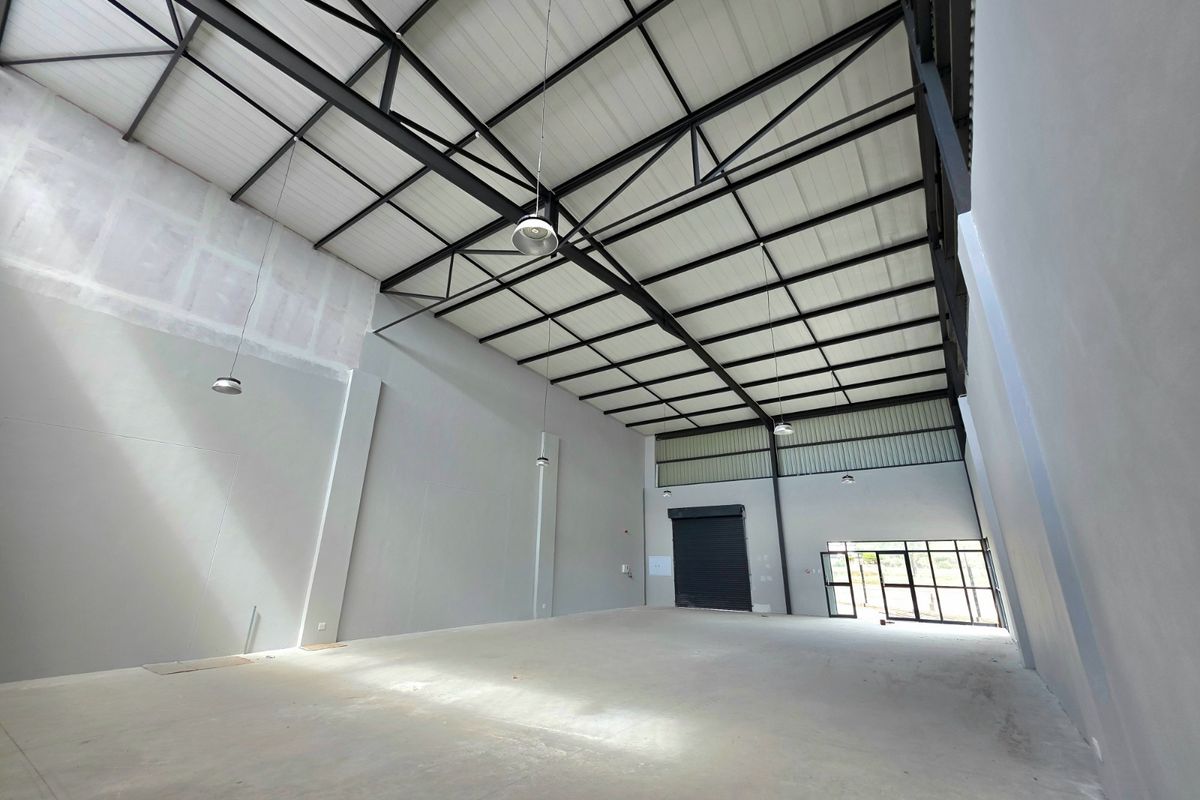 Spacious industrial warehouse unit featuring high ceilings with exposed steel trusses, concrete flooring, and a large roller shutter door for easy access.