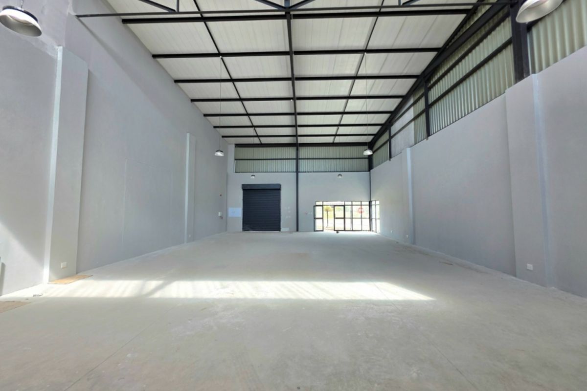 Spacious industrial warehouse unit featuring high ceilings with exposed steel trusses, concrete flooring, and a large roller shutter door for easy access.