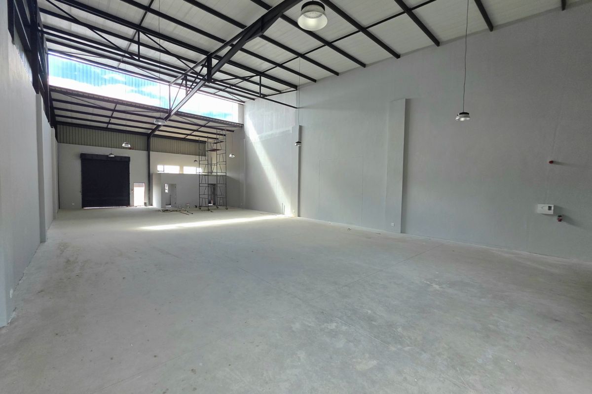 Spacious industrial warehouse unit featuring high ceilings with exposed steel trusses, concrete flooring, and a large roller shutter door for easy access.