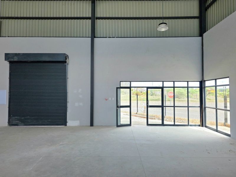 Spacious industrial warehouse unit featuring high ceilings, a large roller shutter door, and expansive glass frontage providing excellent natural light.