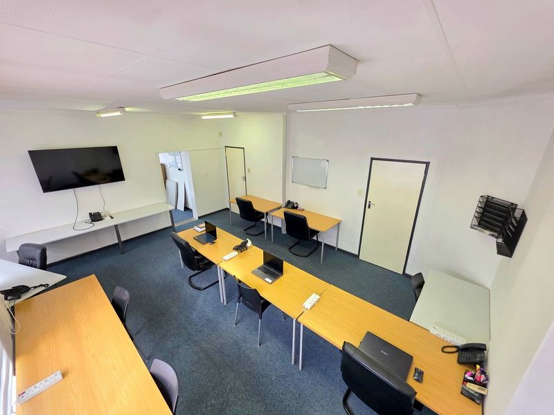 A functional office space featuring carpeted flooring, overhead fluorescent lighting, and built-in wall-mounted shelving, providing a practical environment for professional work.