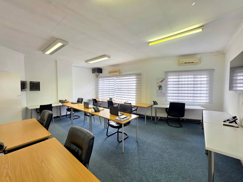 A functional office space featuring carpet flooring, multiple workstations, split-system air conditioning, and roller blinds, with visible ceiling water staining.
