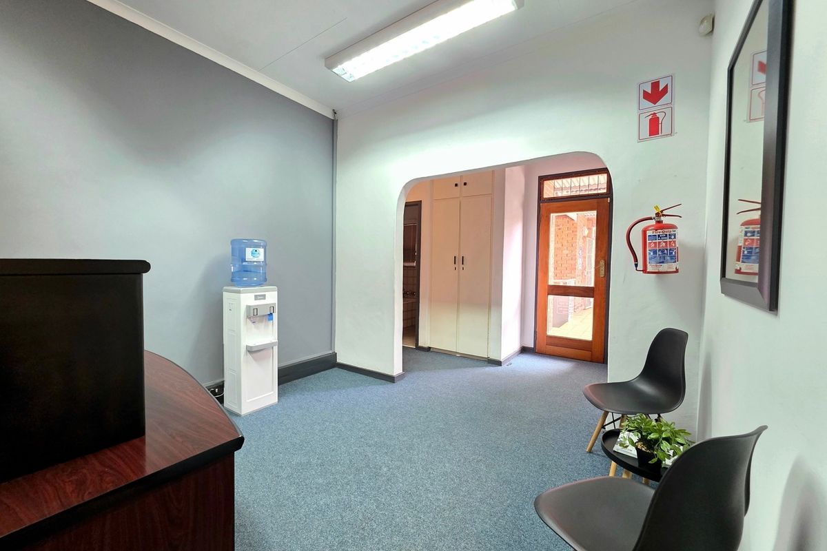 A functional office reception area featuring carpeted flooring, built-in storage cupboards, and an archway leading to the main office space.