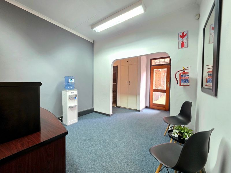 A functional office reception area featuring carpeted flooring, built-in storage cupboards, and an archway leading to the main office space.
