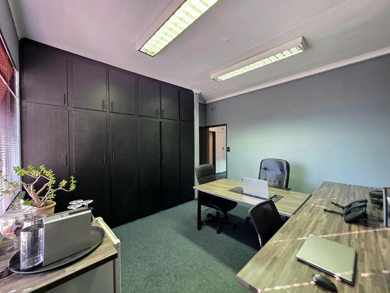 A functional office space featuring extensive built-in black cabinetry, fluorescent overhead lighting, and carpeted flooring, providing a professional work environment.