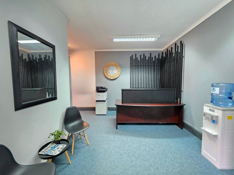 A professional office reception area featuring carpeted flooring, recessed fluorescent lighting, and decorative wall paneling.