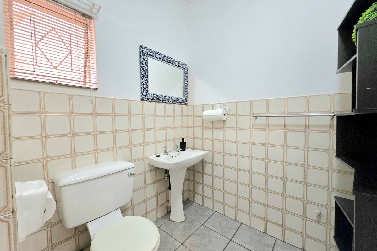 A functional bathroom featuring a pedestal basin, toilet, tiled walls, and tiled flooring, providing essential facilities for an office environment.