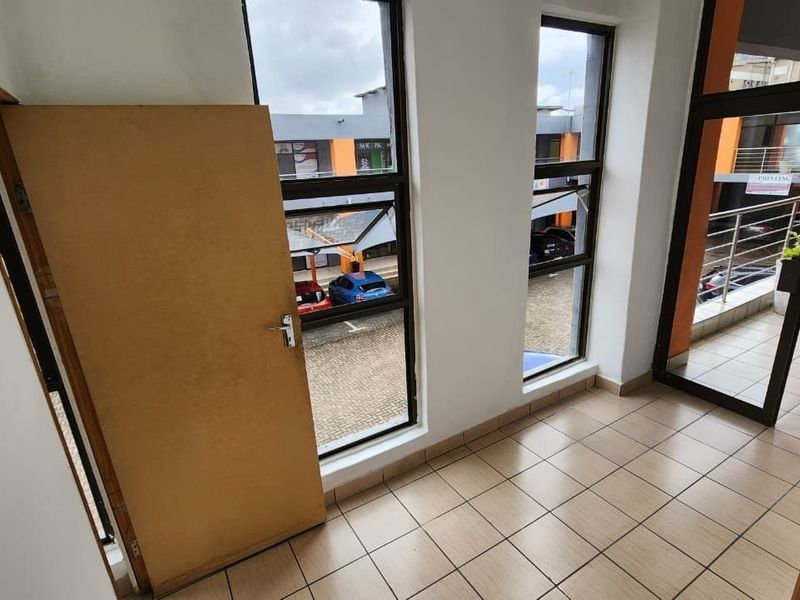 An empty office space featuring tiled flooring, large windows providing natural light, and an integrated access control system at the entrance.