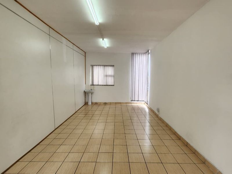 An empty office space featuring tiled flooring, a built-in pedestal sink, fluorescent lighting, and vertical window blinds.