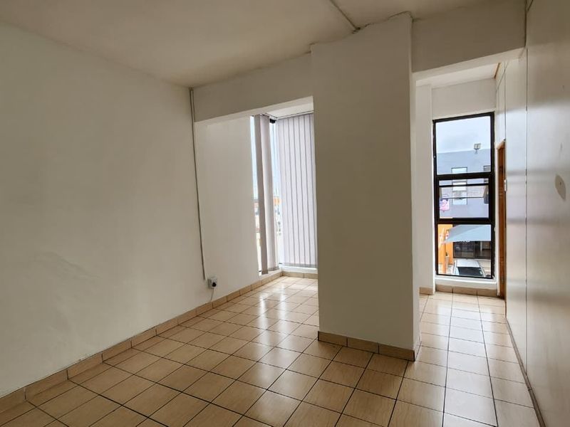 An empty, functional office space featuring tiled flooring, large windows with vertical blinds, and neutral wall finishes.