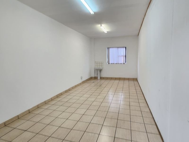 A vacant office space featuring tiled flooring, a small pedestal basin, and fluorescent lighting, offering a clean and functional layout for professional use.