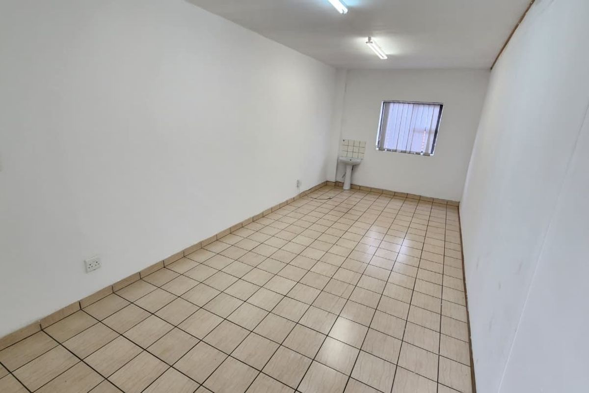 A vacant office space featuring tiled flooring, a small pedestal sink, and fluorescent lighting, suitable for a professional workspace.