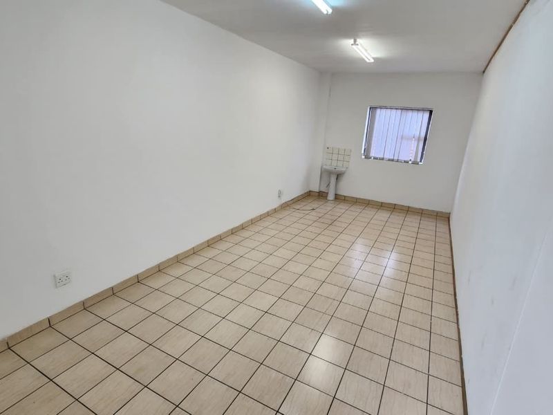A vacant office space featuring tiled flooring, a small pedestal sink, and fluorescent lighting, suitable for a professional workspace.