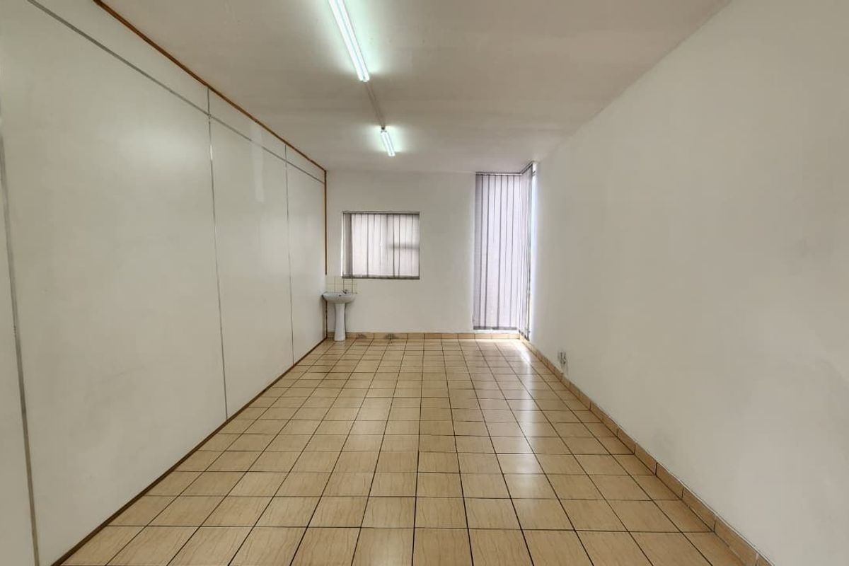 An empty office space featuring tiled flooring, a built-in pedestal sink, and fluorescent lighting, offering a functional layout for professional use.