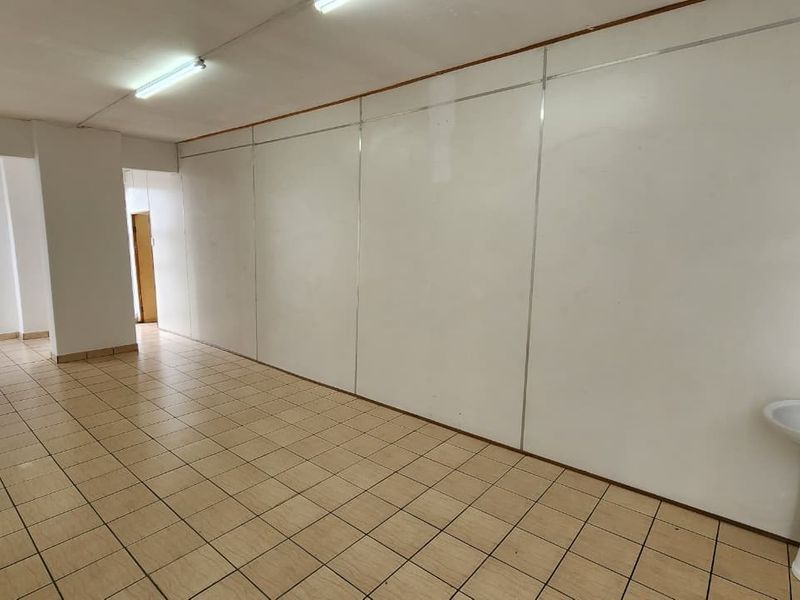 An empty office space featuring ceramic tiled flooring, fluorescent lighting, and a built-in pedestal sink, offering a functional layout for professional use.