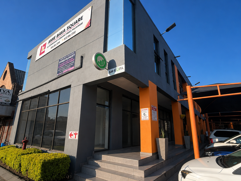 Modern commercial office building facade featuring large glass storefront windows, prominent signage, and a covered parking area for tenants and clients.