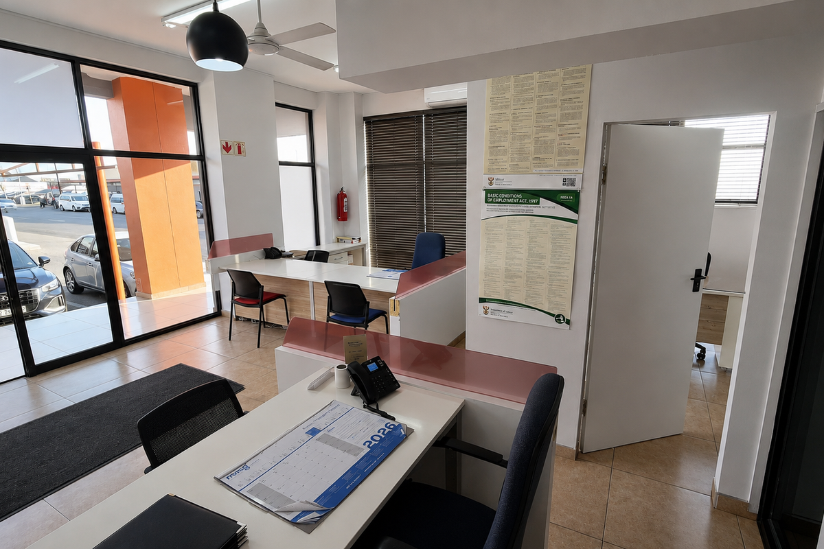 A bright, open-plan office space featuring large glass windows, tiled flooring, built-in desk partitions, and an air conditioning unit.