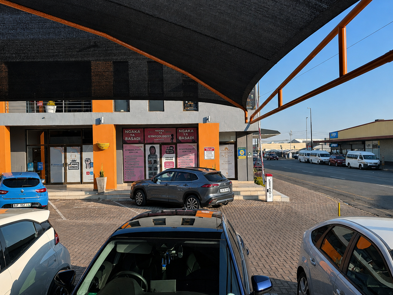 Front exterior view of a commercial office building featuring a paved parking area with overhead shade cloth structures and accessible storefront entrances.