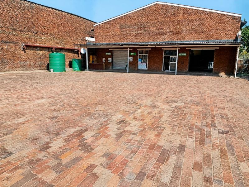 Spacious industrial yard featuring extensive brick paving, exposed brick building facade, roller shutter access, and integrated water storage tanks.