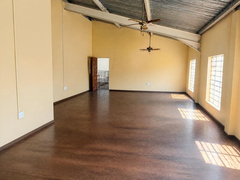 Spacious open-plan office area featuring high vaulted ceilings with exposed metal beams, laminate flooring, and large windows with security bars.