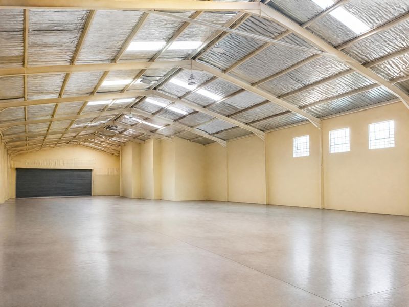 Spacious open-plan office or warehouse area featuring high exposed steel truss ceilings, polished concrete flooring, and natural light from skylights and glass block windows.