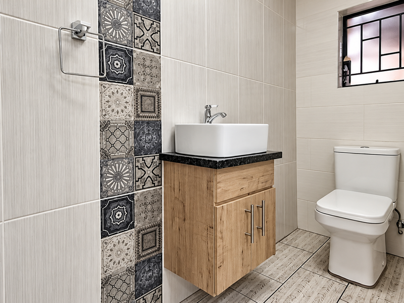 Modern bathroom featuring a wall-mounted wood-finish vanity with a vessel sink, decorative accent tiling, and a clean, contemporary toilet.