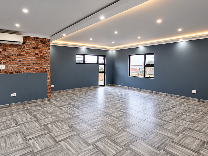 Spacious, modern interior featuring an exposed brick wall, recessed ceiling lighting with cove accents, tiled flooring, and a wall-mounted air conditioning unit.