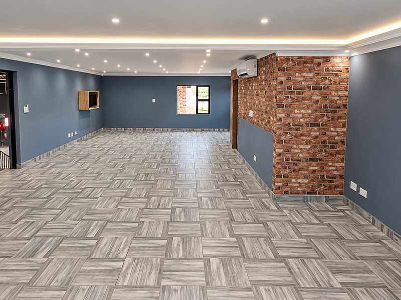 Spacious open-plan industrial office area featuring modern tiled flooring, an exposed brick feature wall, recessed ceiling lighting, and integrated air conditioning.