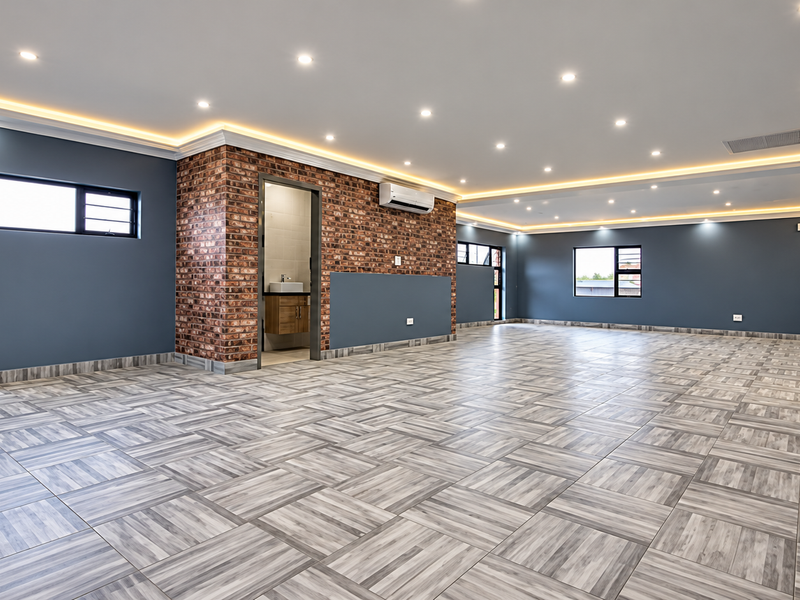 Spacious open-plan industrial-style area featuring modern recessed and cove lighting, exposed brick accents, tiled flooring, and an integrated air conditioning unit.