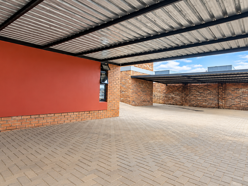 A spacious, well-maintained industrial-style covered parking area featuring brick walls, a corrugated metal roof, and durable paved flooring.