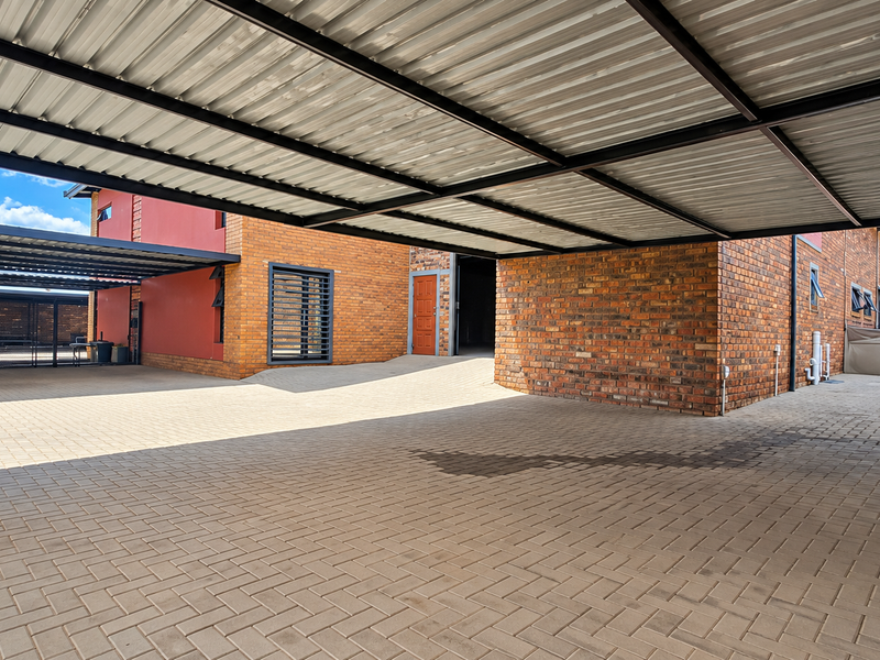 Spacious industrial-style exterior area featuring a large covered carport, paved driveway, and durable exposed brick facade construction.